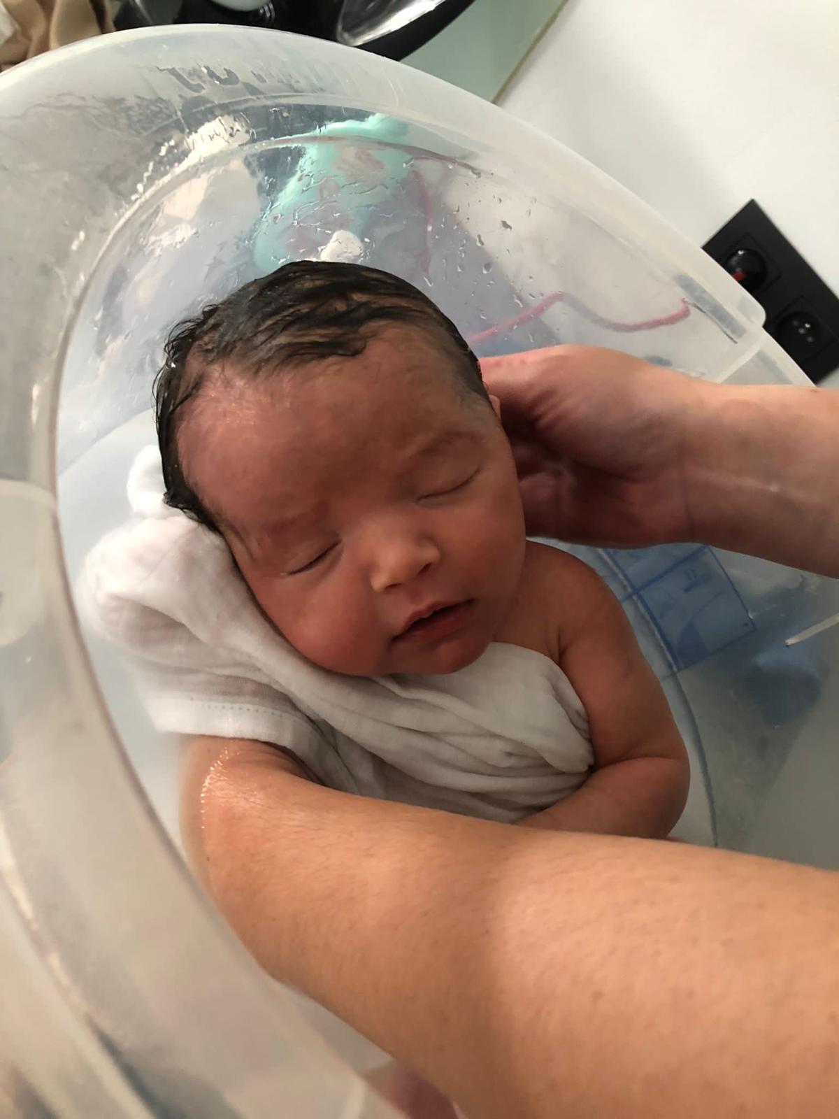 Slapende pasgeboren baby wordt voorzichtig in bad ondersteund